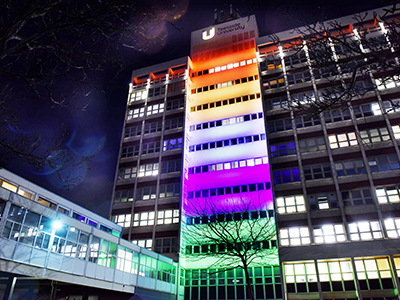 The Tower building lit up in rainbow colours to celebrate Pride month. Link to Stonewall recognition for Teesside University.