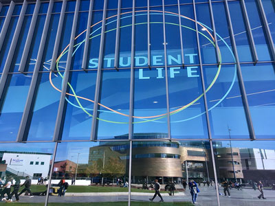 A view of the Student Life Building in the campus heart of Teesside University. The Curve building is reflected in the windows.. Link to Welfare Week, 24-28 March 2025.