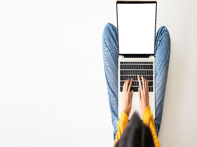 An overhead view of a person using a laptop. They are wearing blue trousers and a yellow jumper.. Link to Turn Up and Discover: Searching for Your Assignment (Undergraduate) - Monday 31 March.