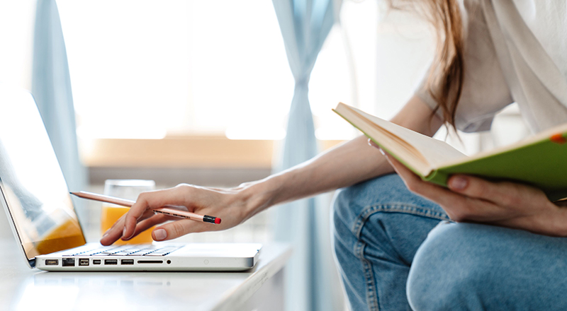 Student working at a laptop, with notebook in hand